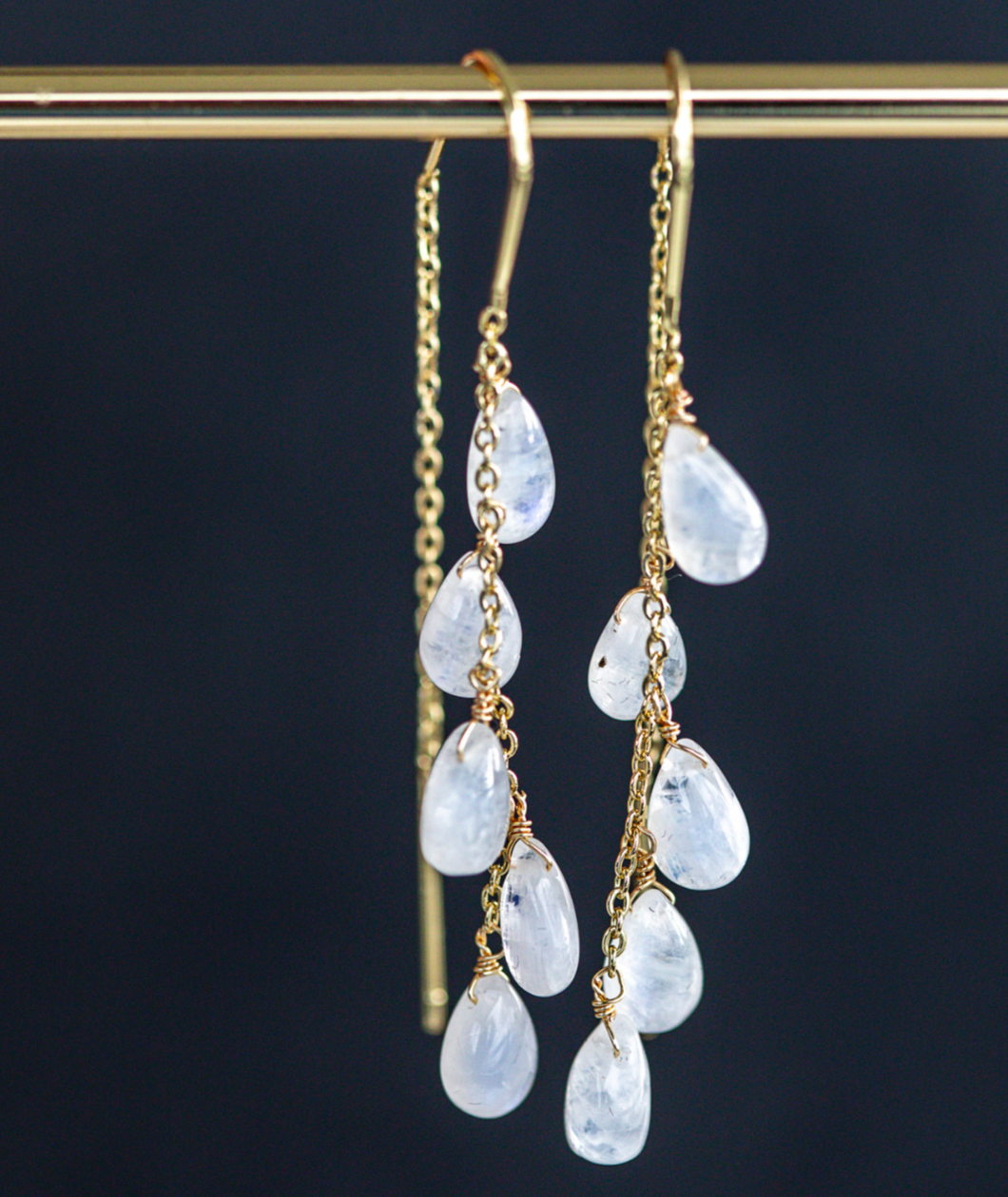 Gold earrings with teardrop-shaped gemstones on a dark background