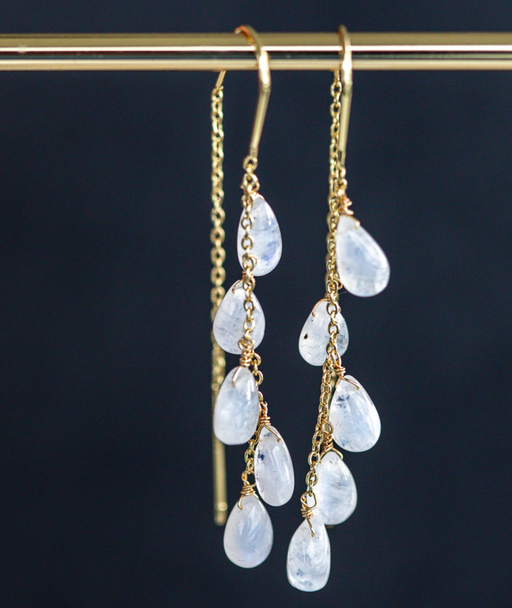 Gold earrings with teardrop-shaped gemstones on a dark background