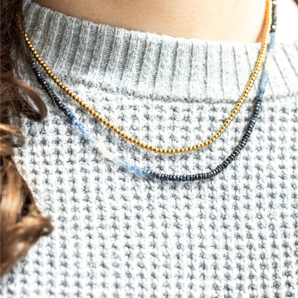 Necklace with blue and gold beads worn by a person in a gray sweater.