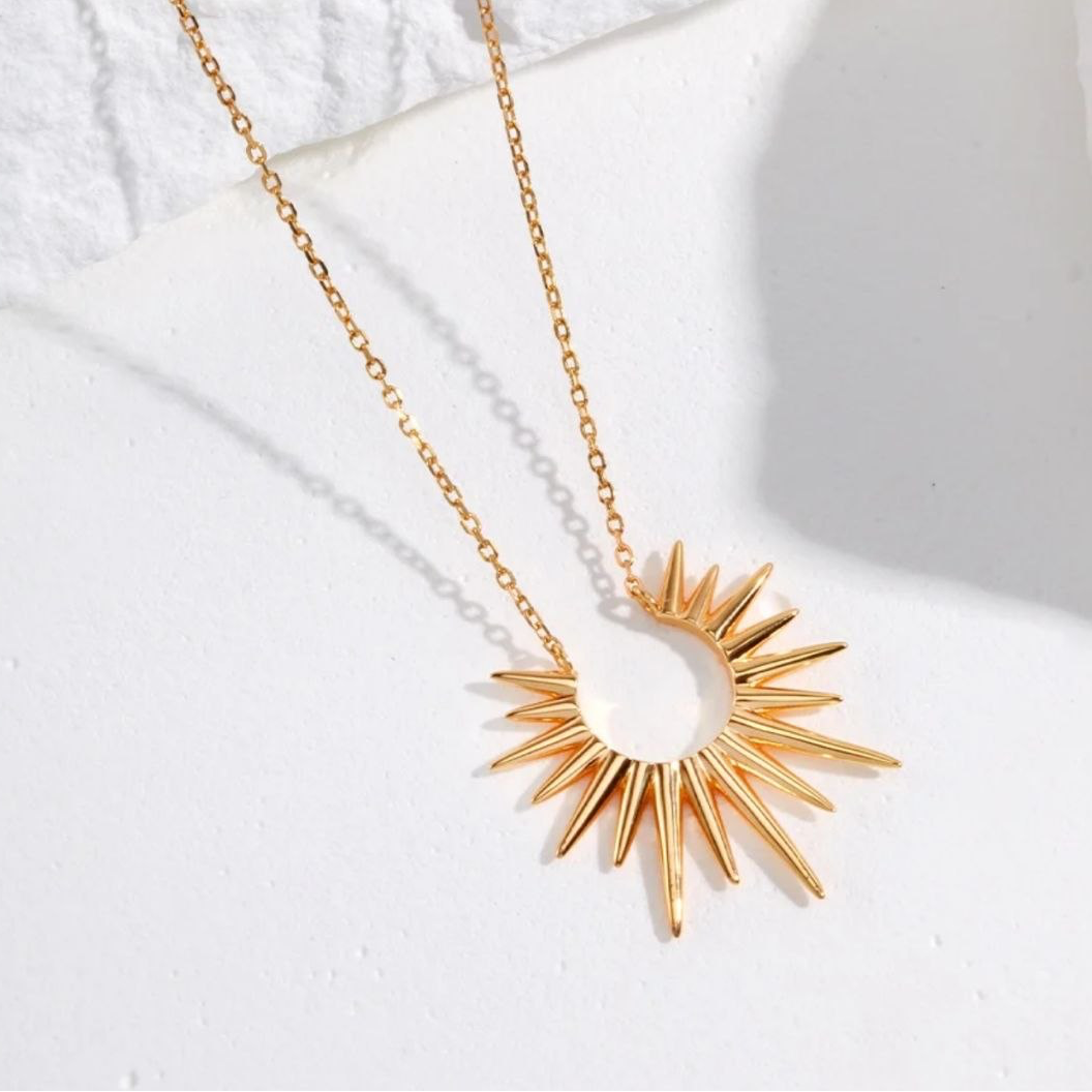 Gold necklace with a sunburst pendant on a white background
