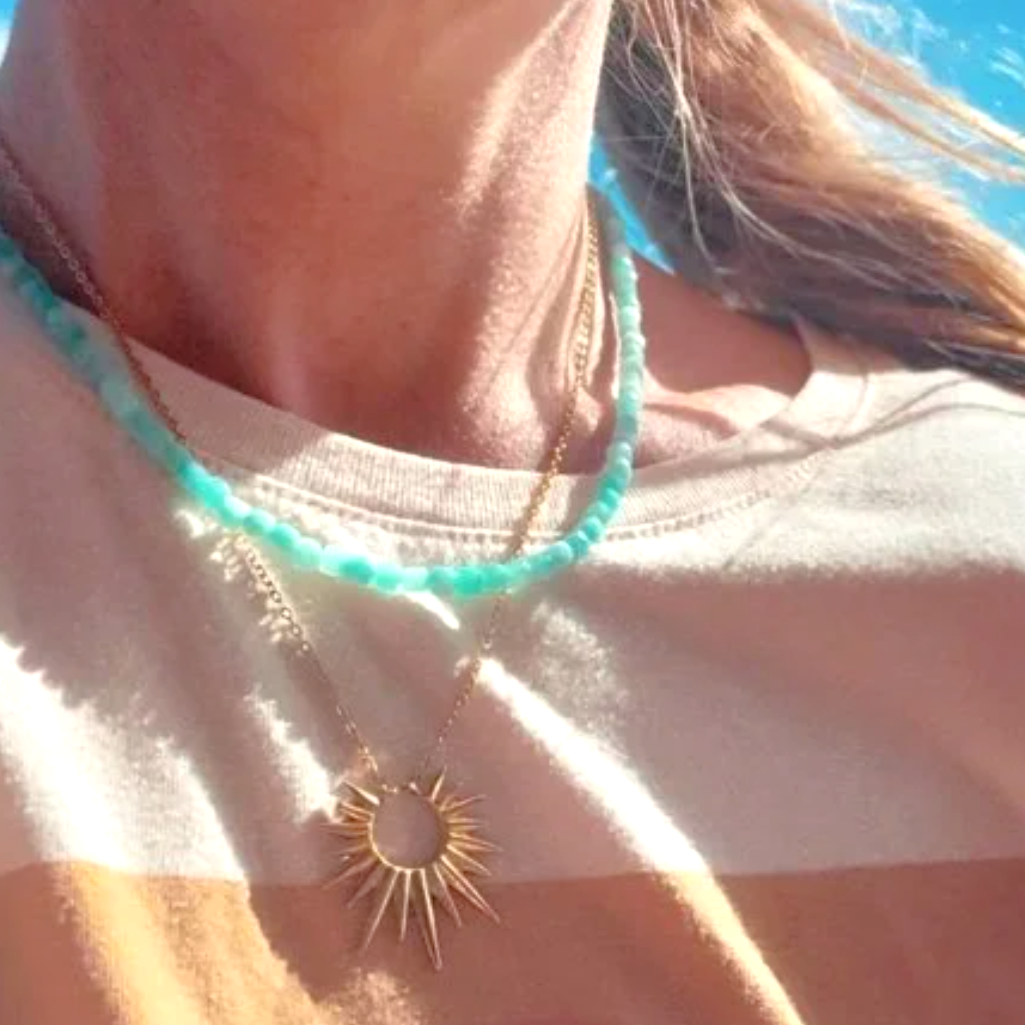 Close-up of a necklace with a sun design worn by a person against a blue sky.