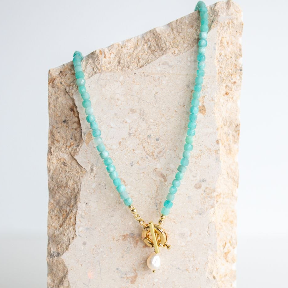 Turquoise beaded necklace with a gold clasp on a textured stone surface