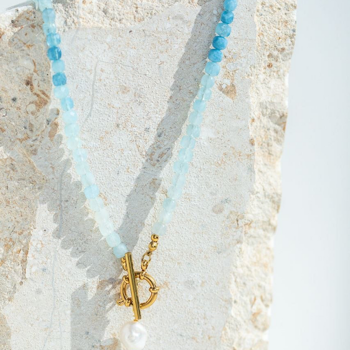 Necklace with blue beads and gold clasp on a textured stone surface