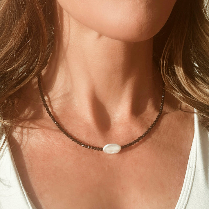 Model wearing a dainty black beaded necklace with a beautiful pearl winter jewelry 