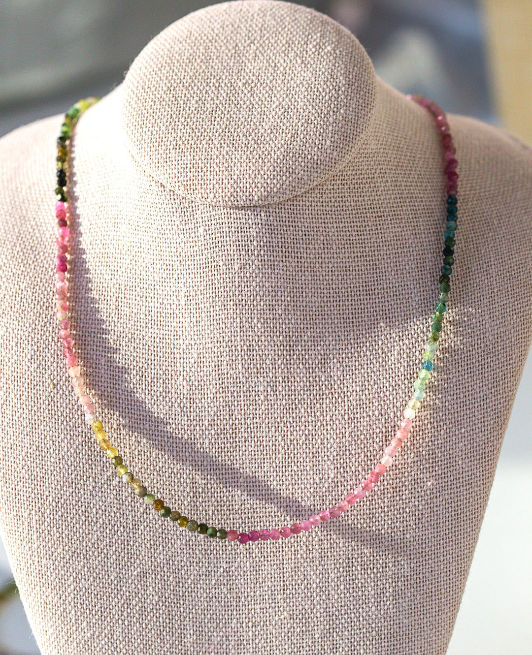 Necklace with multicolored beads on a gray mannequin bust.