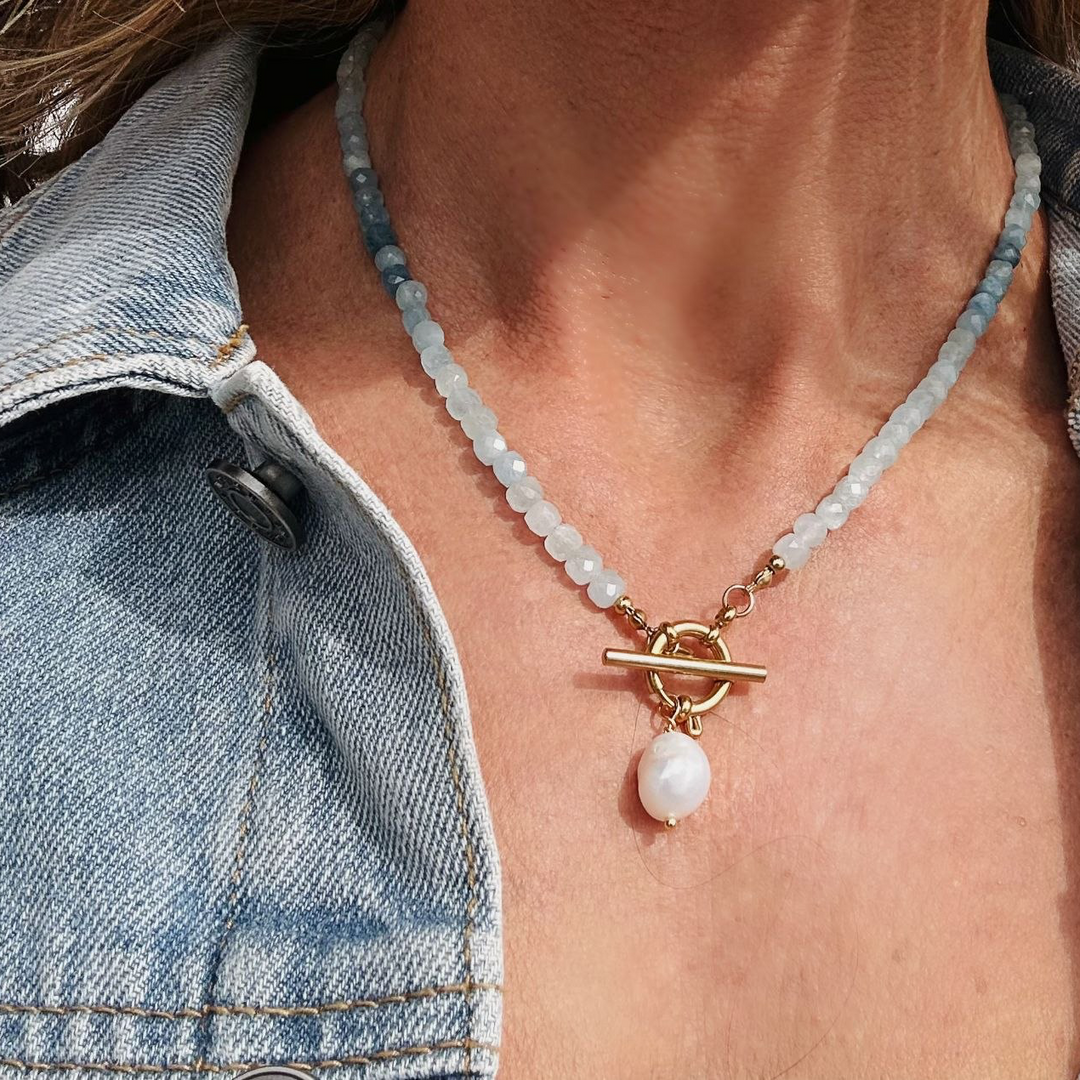 Necklace with a pearl pendant worn by a person in a denim jacket.