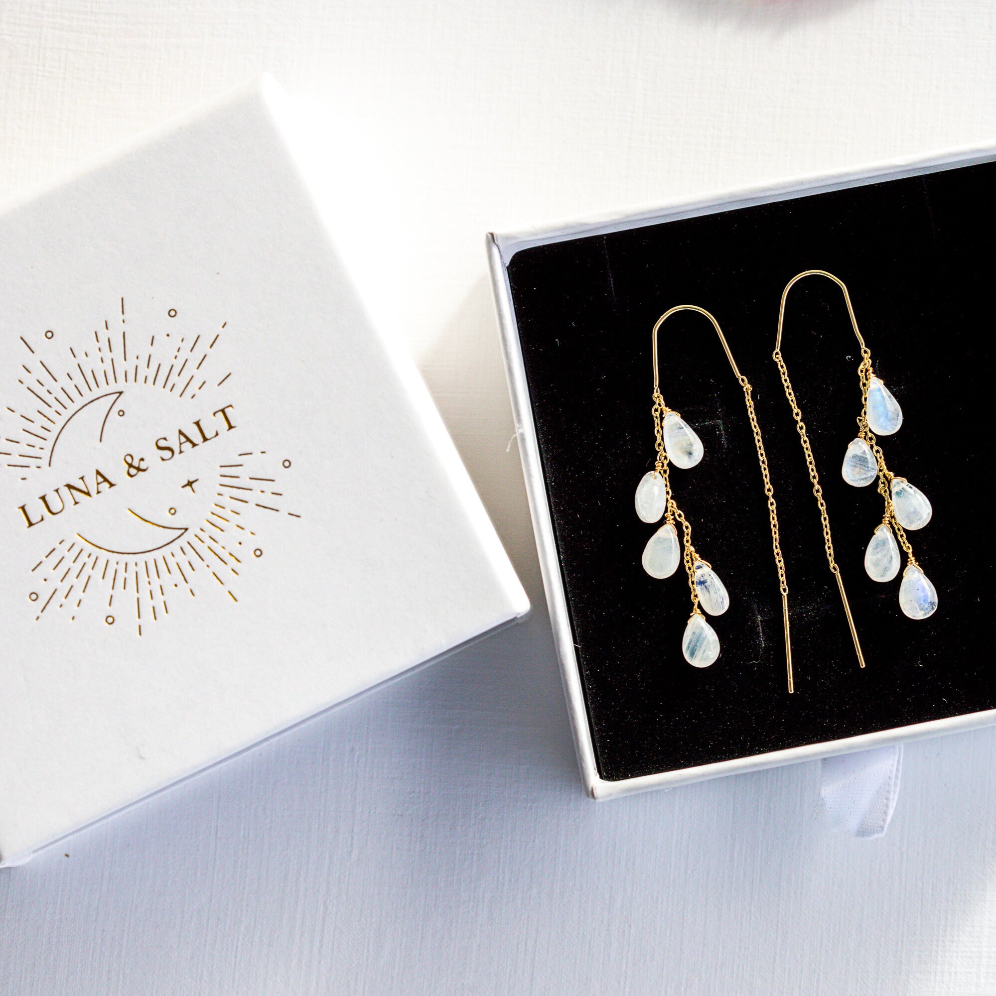 Gold and white teardrop earrings in a box with Luna & Salt branding.