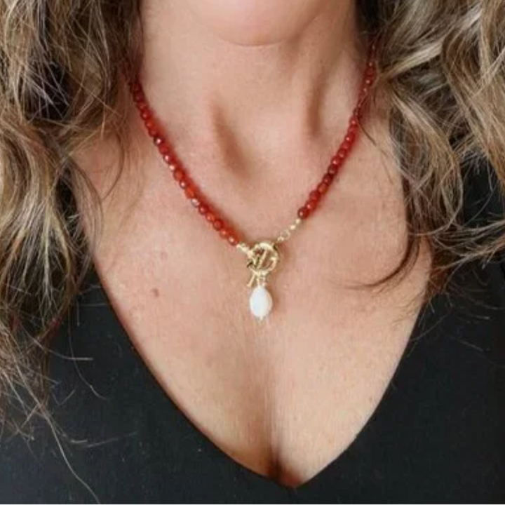Person wearing a red gemstone beaded necklace with a pearl pendant