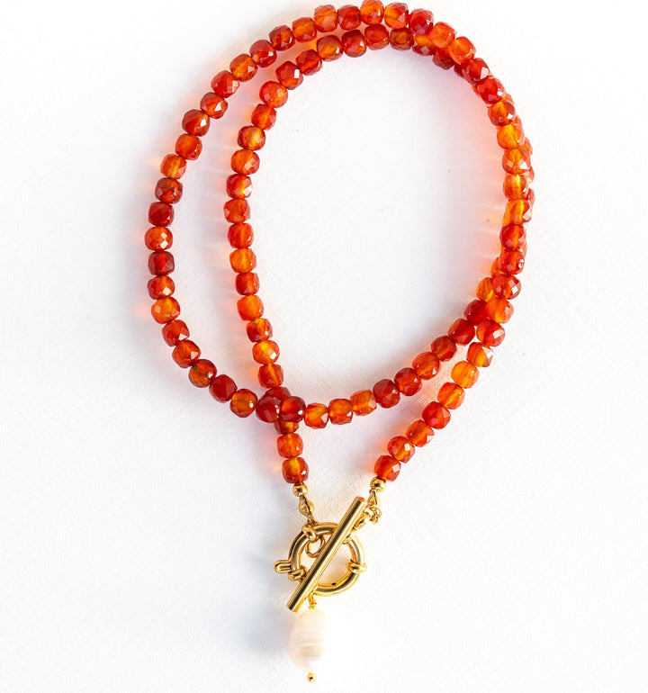 Necklace with orange beads and a gold toggle clasp on a white background