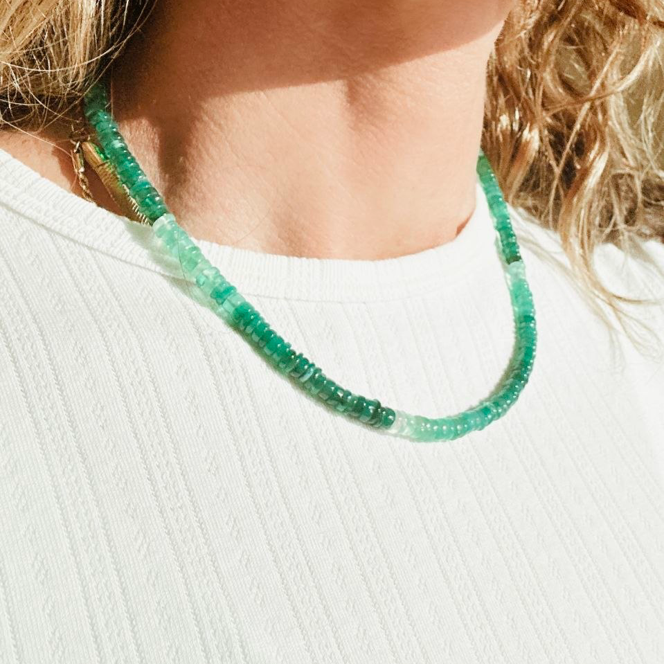 Close-up of a person wearing a green beaded necklace against a white background