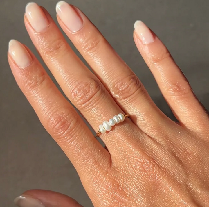 Hand wearing a pearl ring with a neutral background