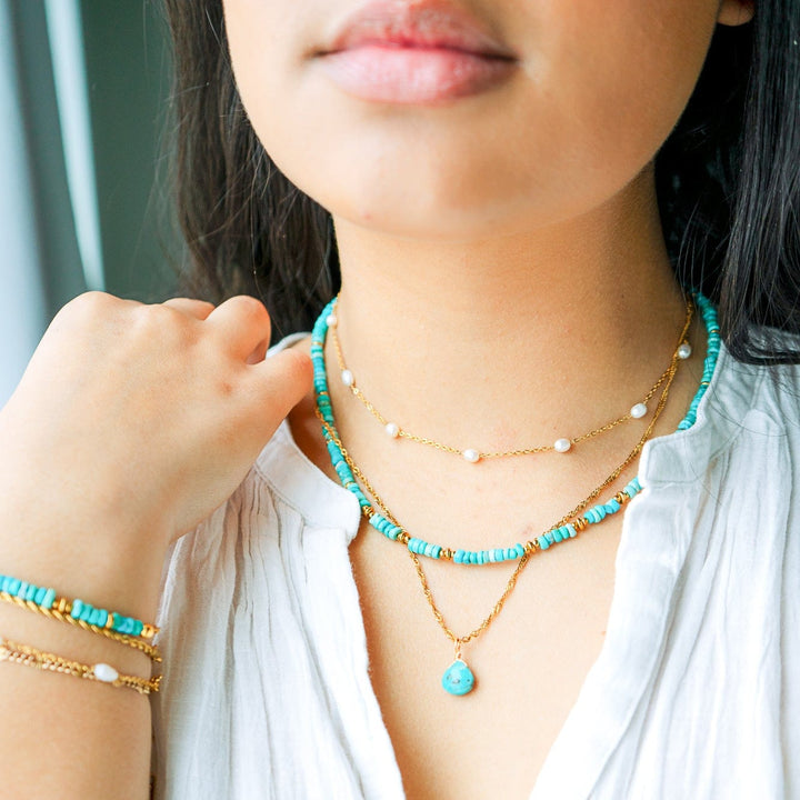 Person wearing multiple necklaces and bracelets with a focus on turquoise jewelry.