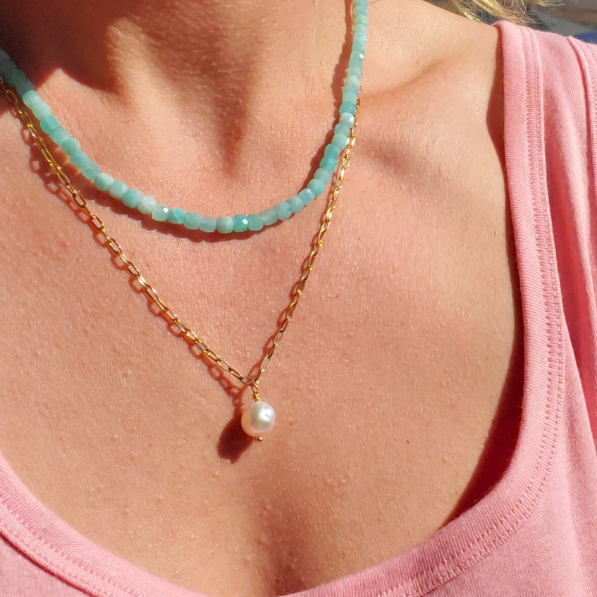 Close-up of a person wearing two necklaces with a pink top.