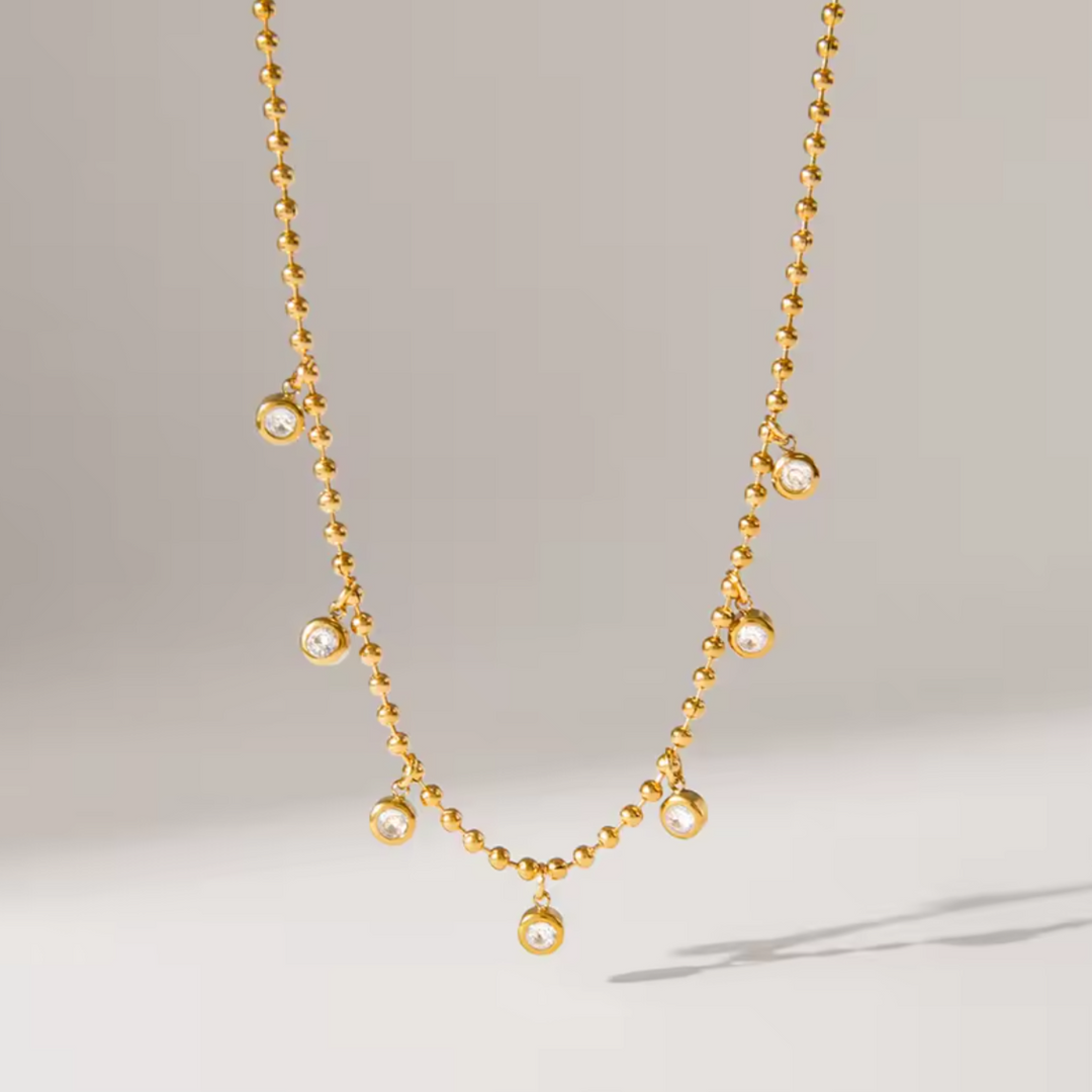 Gold necklace with small zircon charms on a light gray background
