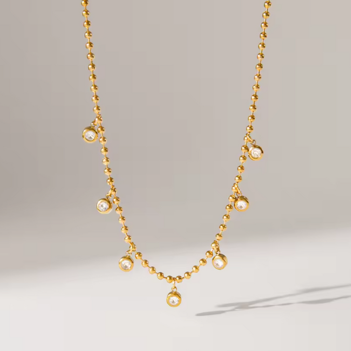 Gold necklace with small zircon charms on a light gray background