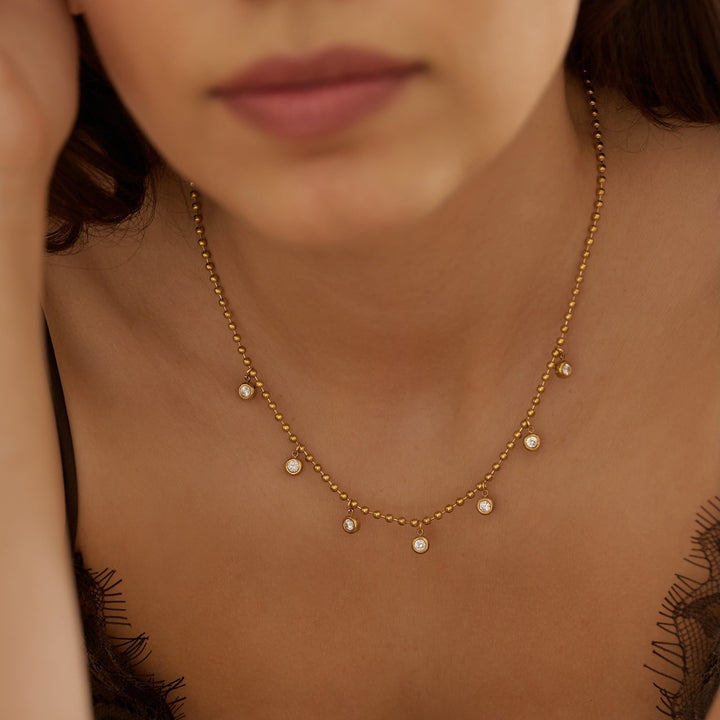 Close-up of a woman wearing a delicate gold necklace with small beads and cubic zirconia bezel charms 