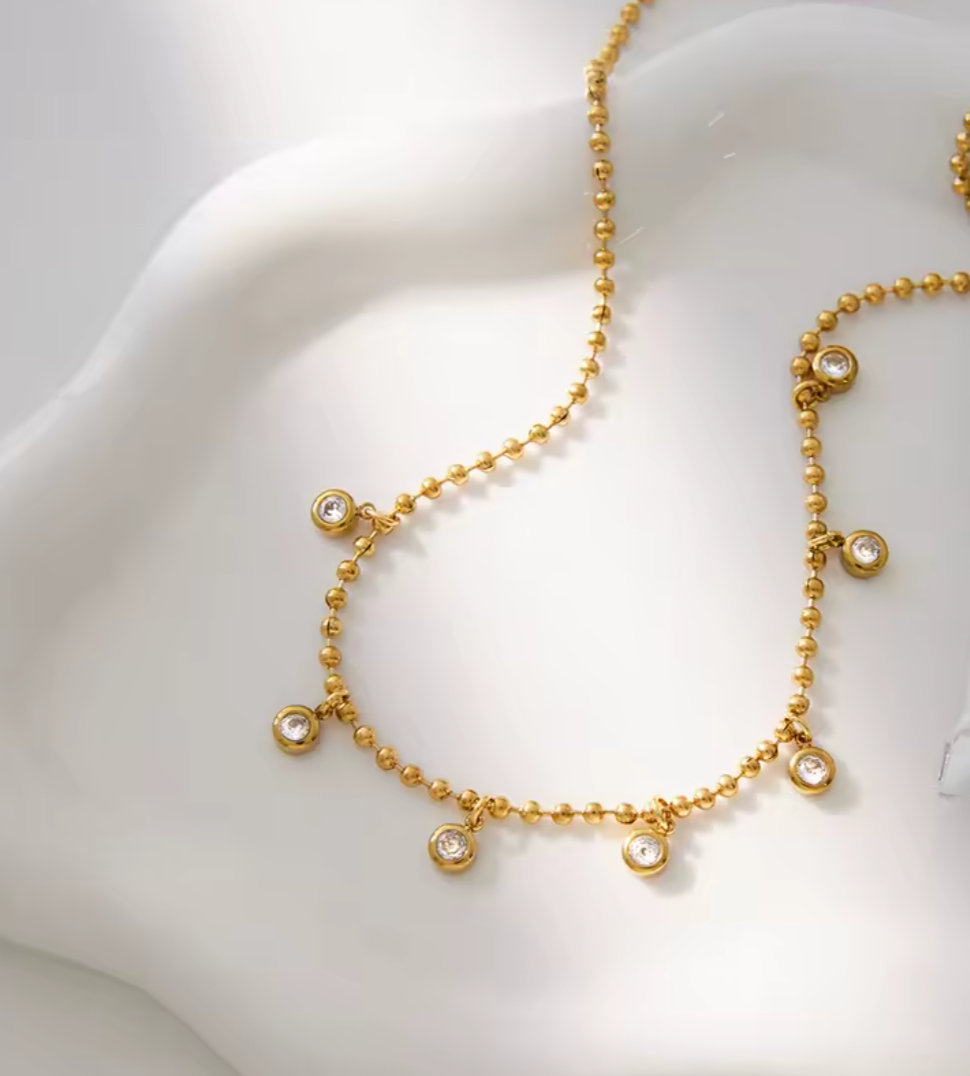 Gold necklace with cubic zirconia bezel drops beads on a mannequin bust.