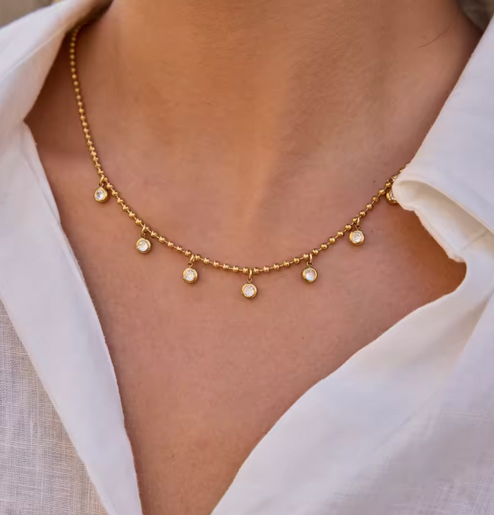 Gold necklace with small round pendants on a person wearing a white shirt.