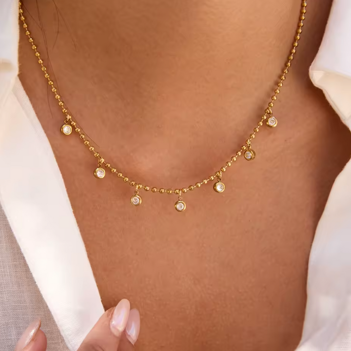 Gold necklace with small pendants on a person wearing a white shirt.