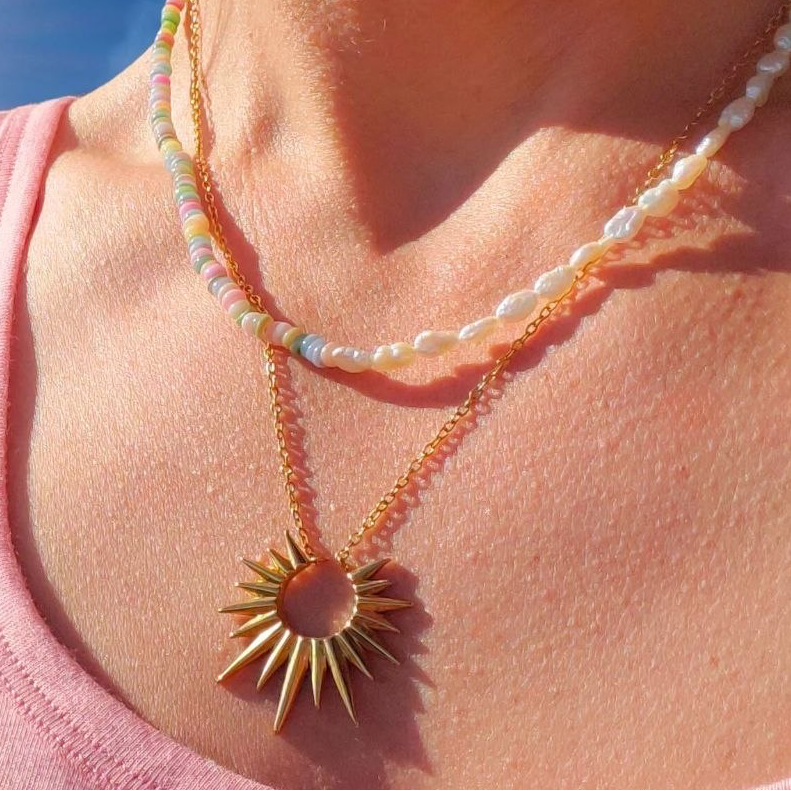Necklace with a sun-shaped pendant worn by a person against a blue sky.