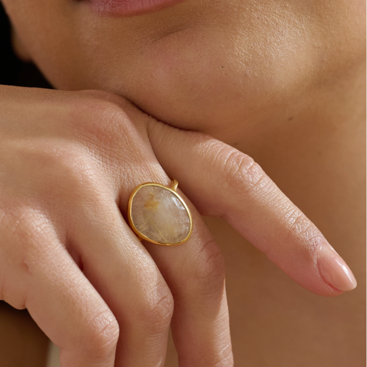 Close-up of a hand wearing a gold vermeil cocktail gemstone ring with a large faceted stone on a neutral background