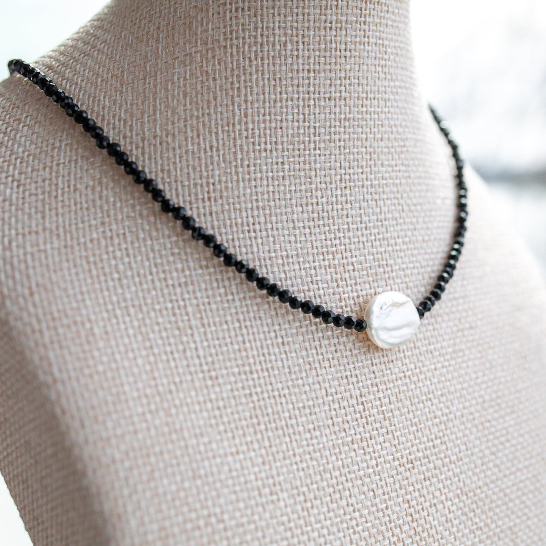 A black beaded necklace with a single white irregular shell pendant, winter jewelry 