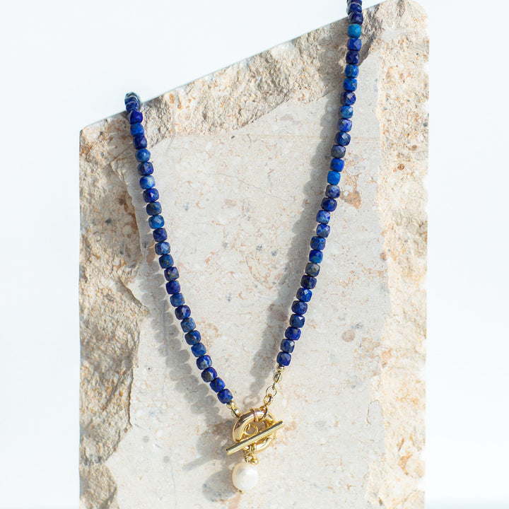 Blue beaded necklace with a gold clasp on a stone surface