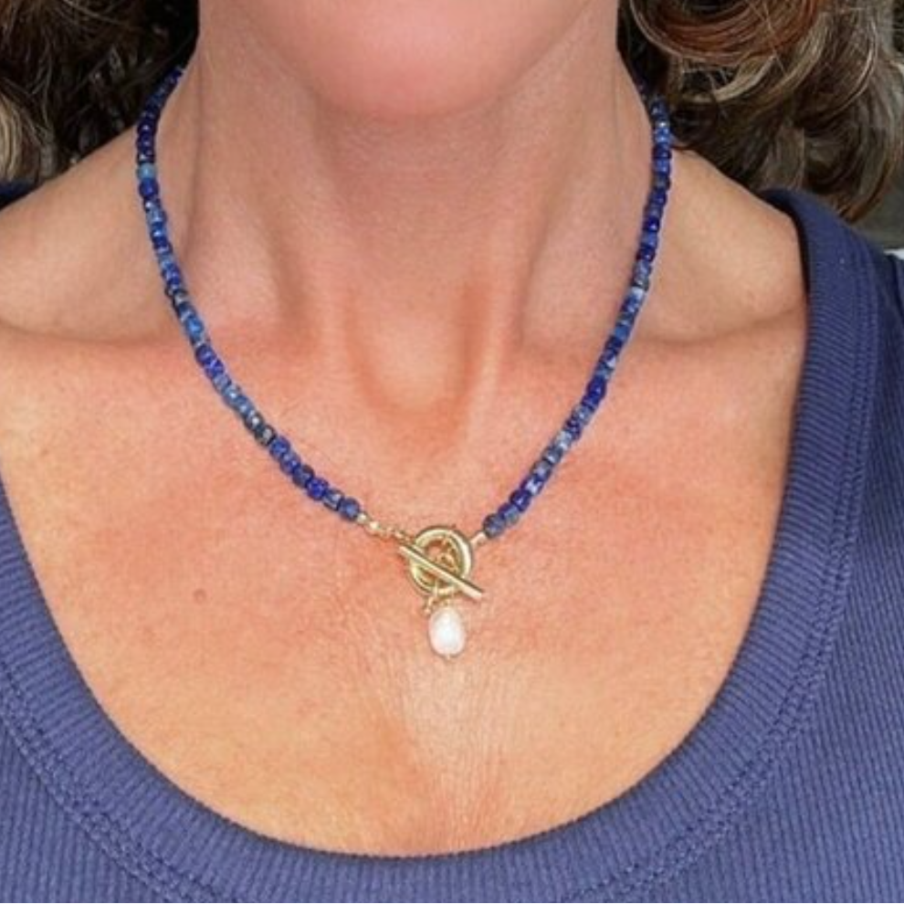 Woman wearing a blue beaded necklace with a heart pendant and pearl drop.