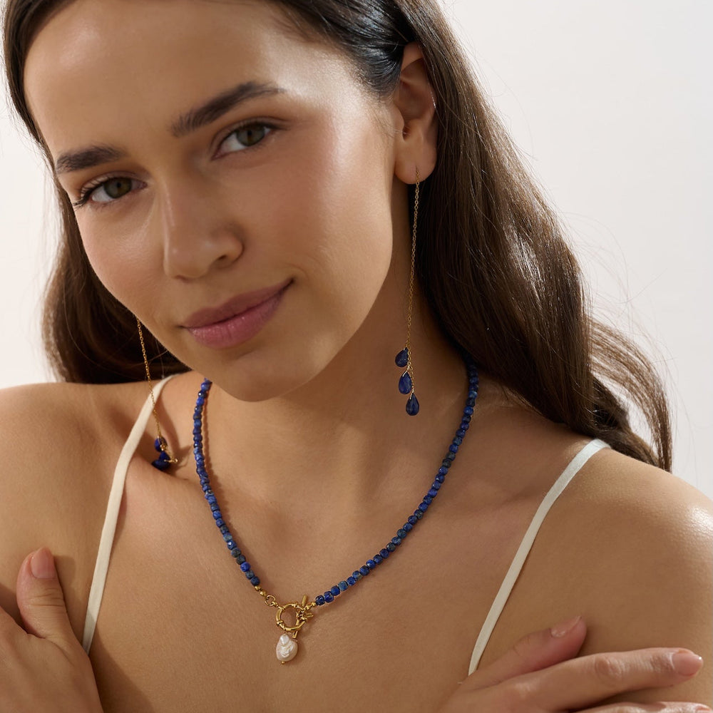 Woman wearing a blue lapis lazuli beaded necklace with a white top against a plain background
