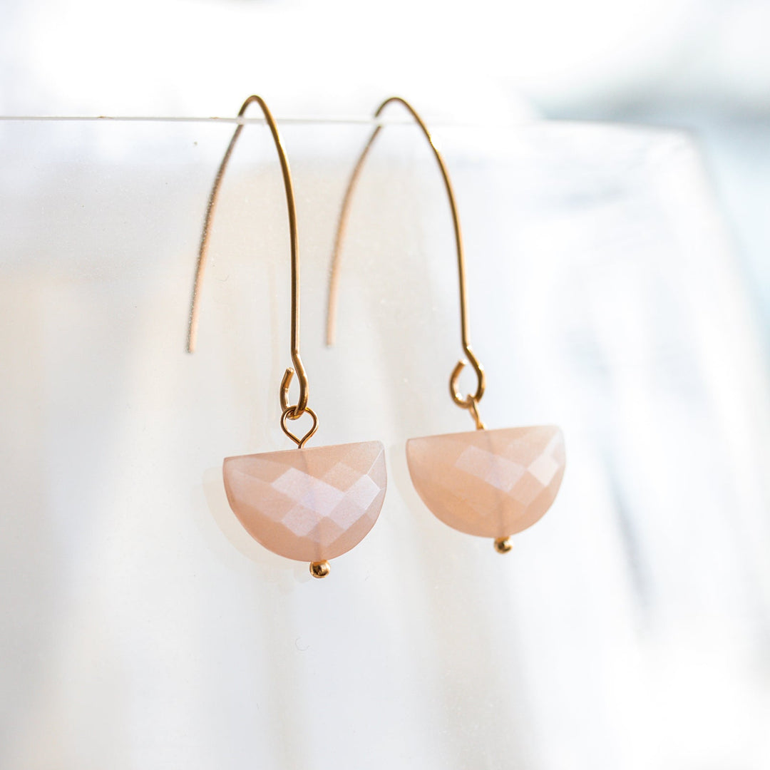 Pair of earrings with pinkish peach semi-circular faceted gemstones on a blurred background on gold non tarnish hooks 