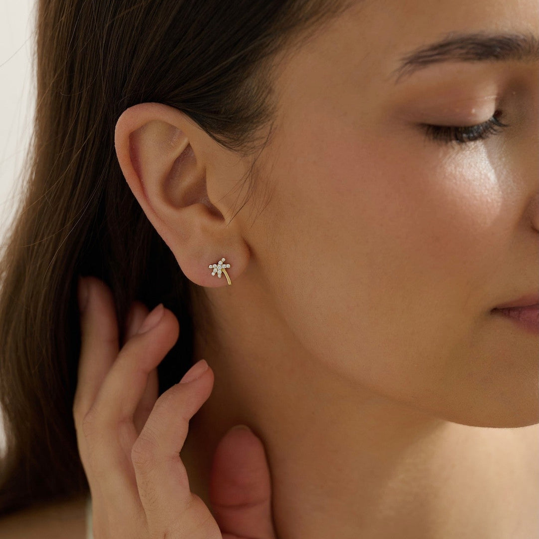 Close-up of a woman wearing dainty palm tree stud earrings tropical vacation jewelry 