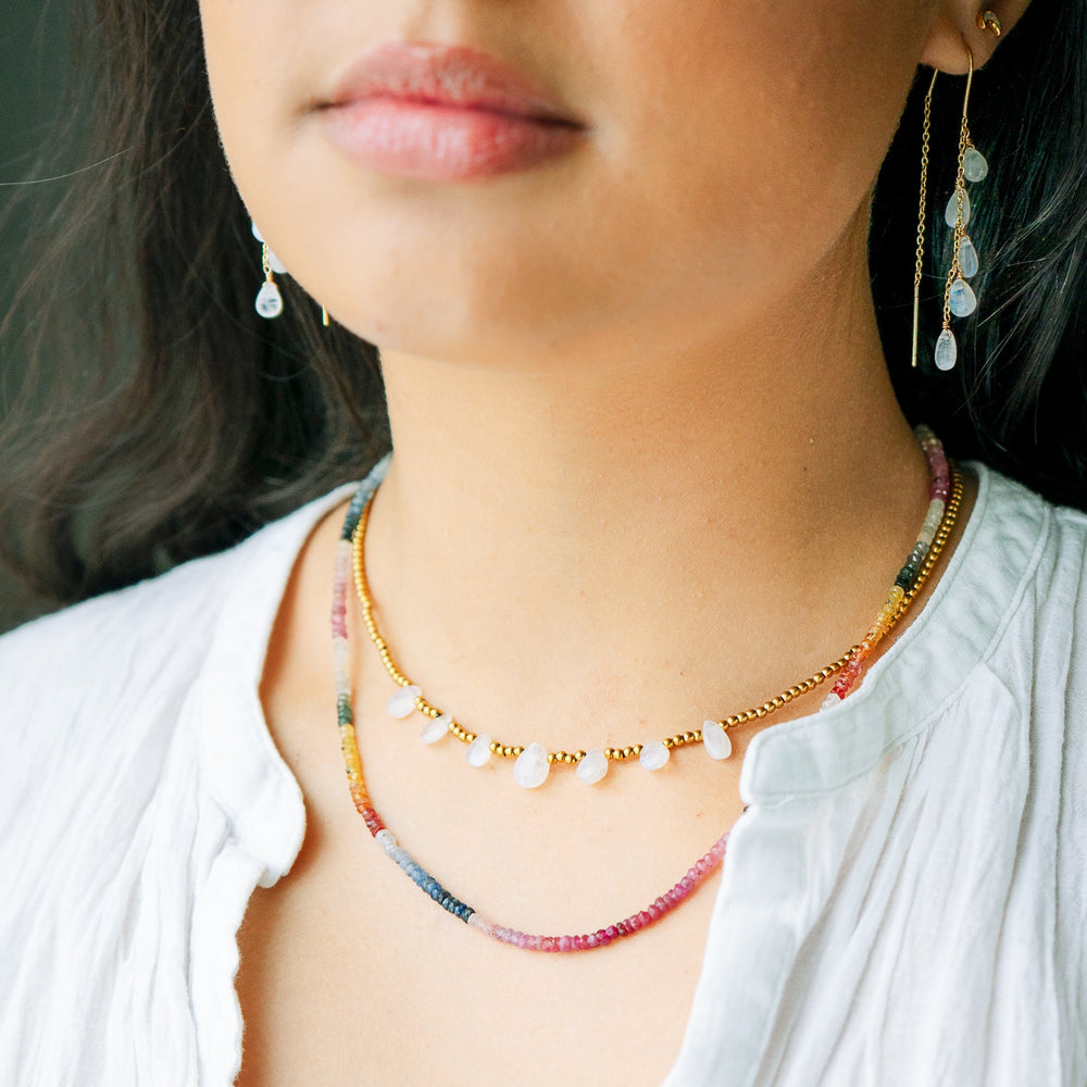 Close-up of a person wearing a colorful sapphire necklace and moonstone earrings.