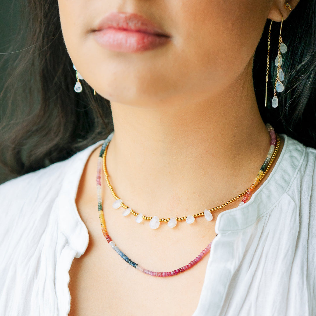 Close-up of a person wearing a colorful sapphire necklace and moonstone earrings.