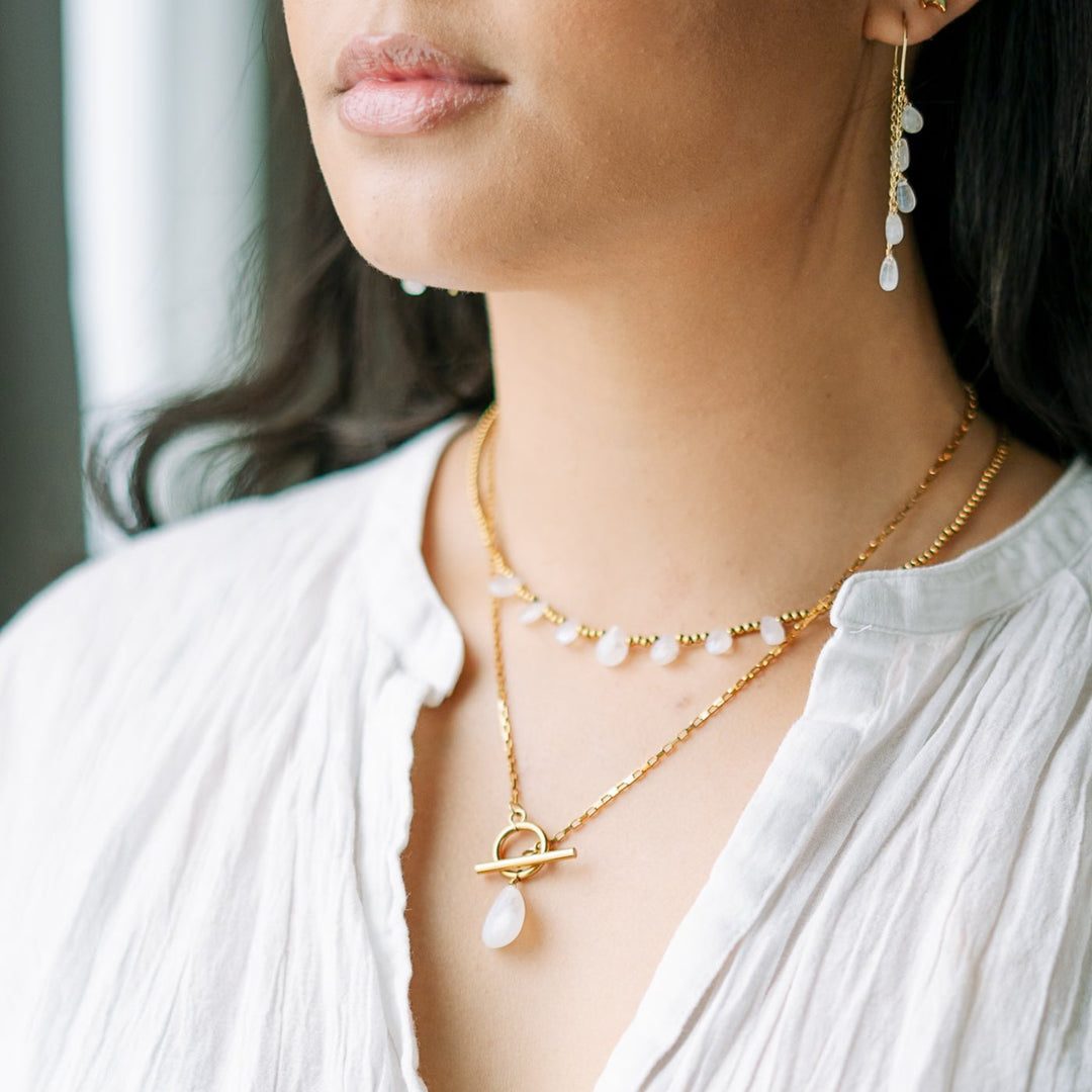 Close-up of a woman wearing gold blue flash moonstone necklaces and earrings with a blurred background