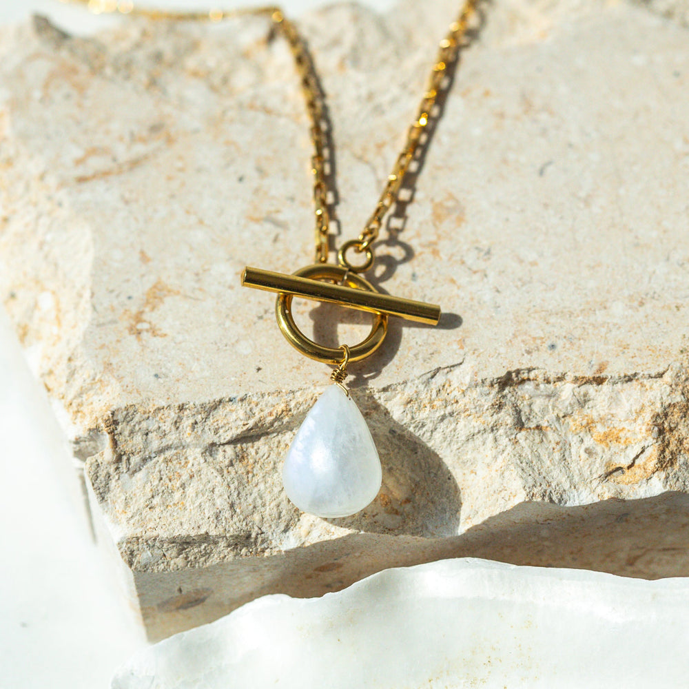 Gold necklace with a teardrop-shaped moonstone on a stone surface