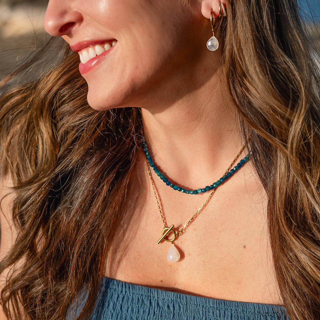 Woman wearing a necklace with a blue beaded strand and moonstone blue flash pendant, outdoors.