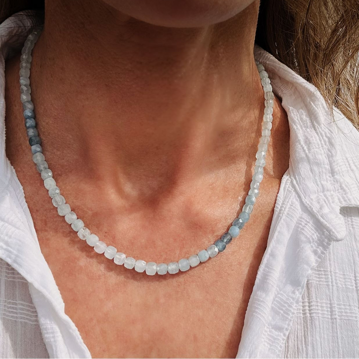 Necklace with small beads worn by a person in a white shirt.