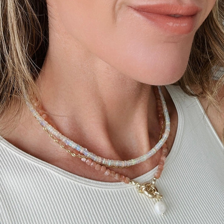 Close-up of a woman wearing a delicate fire opal necklace with a white top.