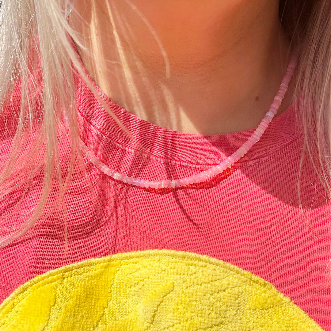 Person wearing a pink shirt with a hot pink necklace opal necklace 