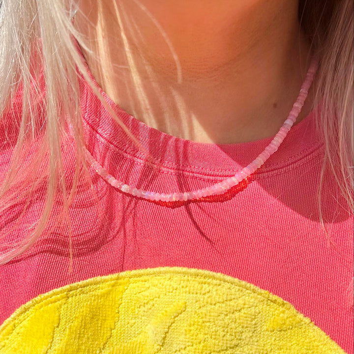 Person wearing a pink shirt with a hot pink necklace opal necklace 