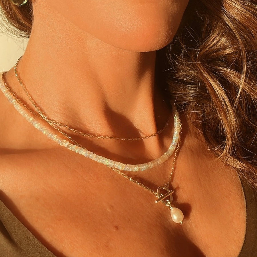 Close-up of a woman wearing a necklace with a pearl pendant against a neutral background