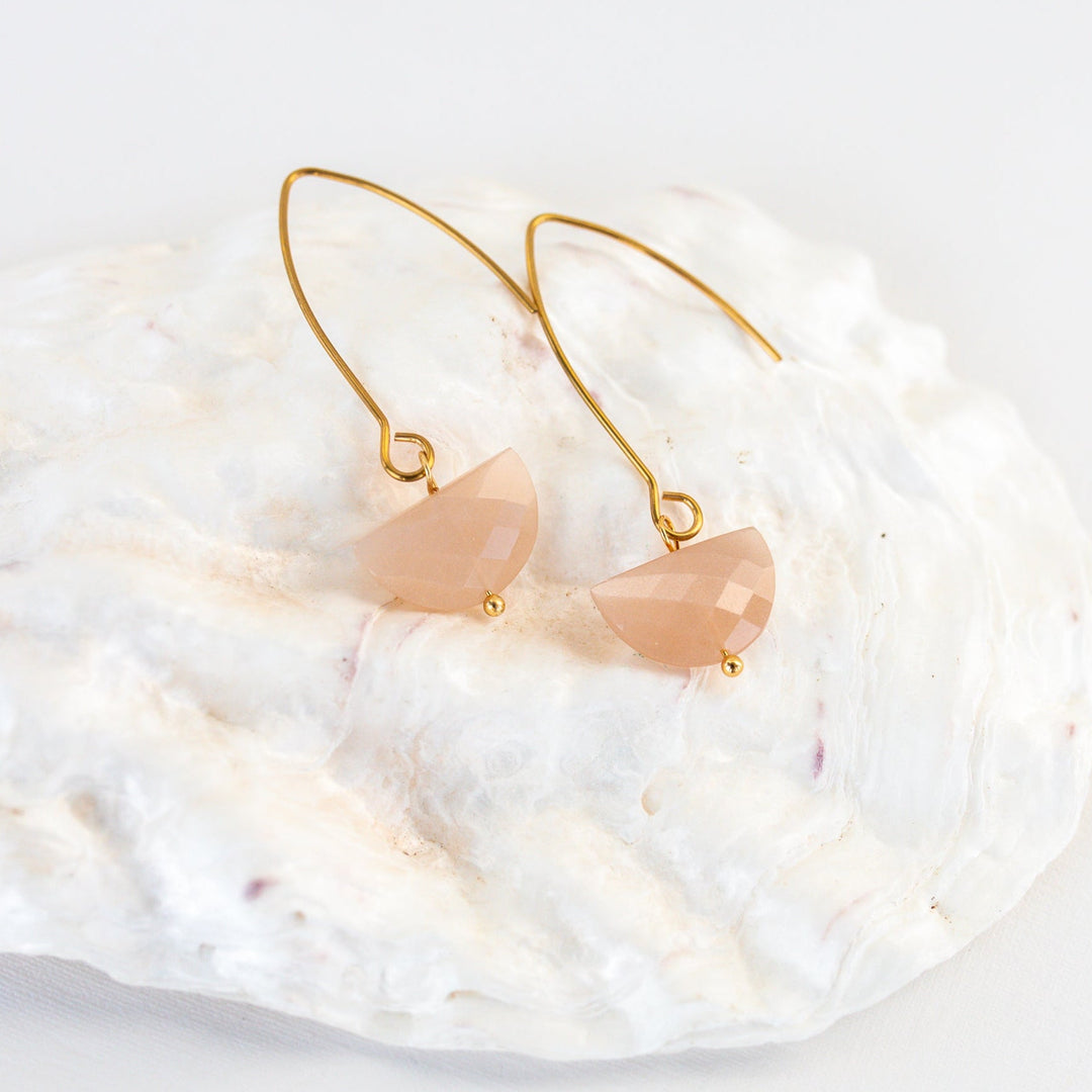 Gold dangle earrings with peach-colored heart-shaped stones on a white background