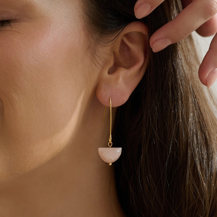 Close-up of an ear wearing a delicate gold threader style earring with a peach faceted moonstone and her hand adjusting hair.