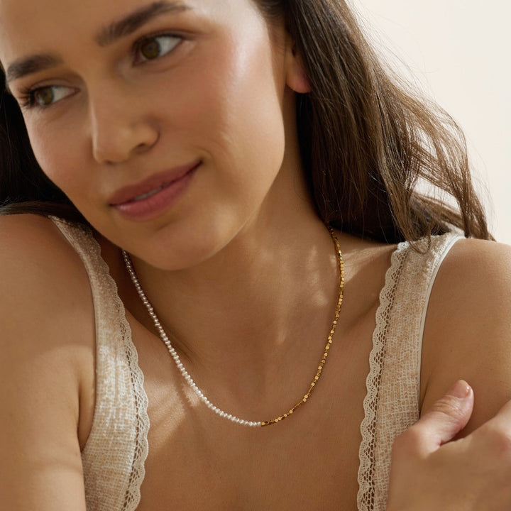 Woman wearing a pearl and sparkle gold beaded necklace against a neutral background waterproof jewelry 