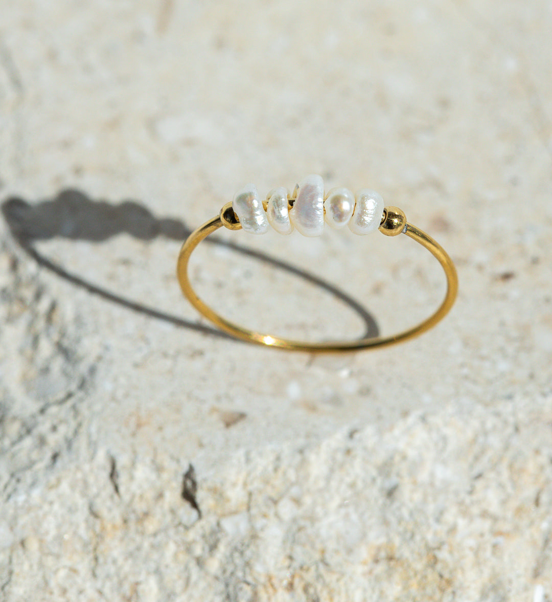 Gold ring with pearls on a textured beige surface
