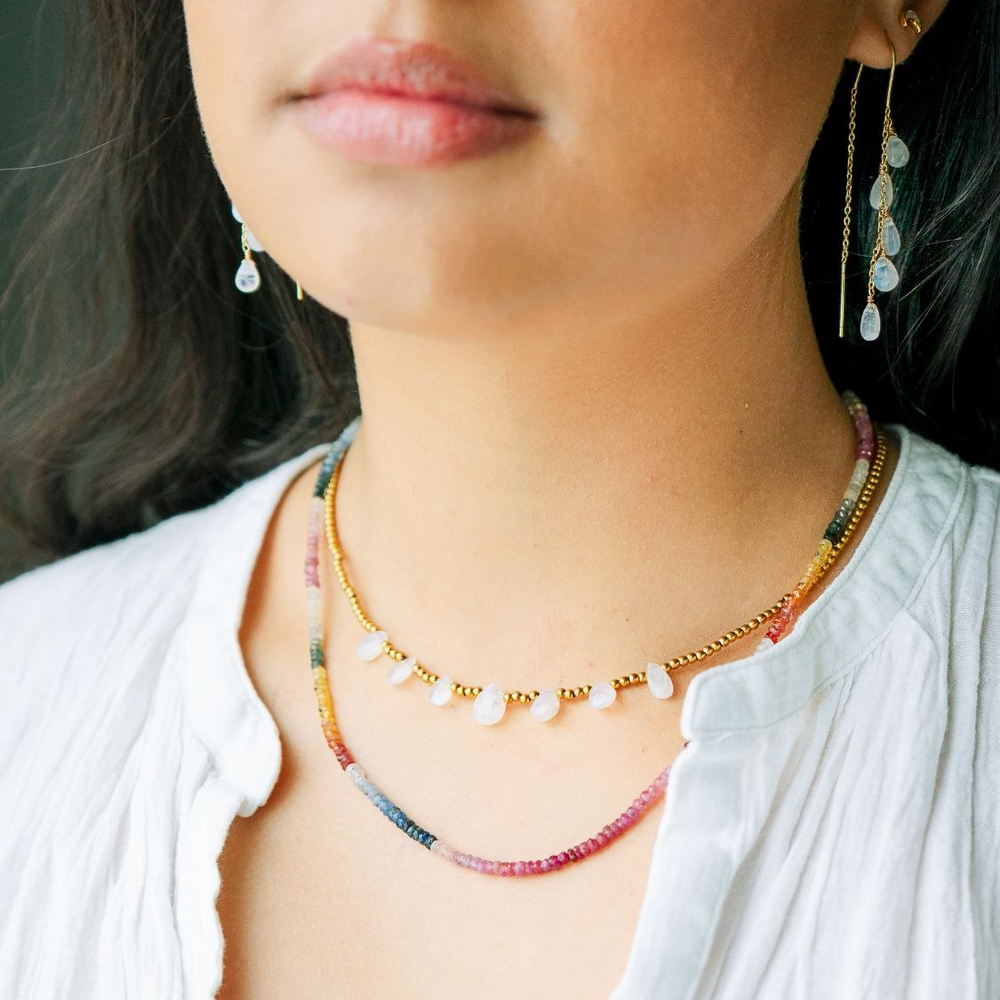 Close-up of a person wearing a colorful sapphire beaded necklace and earrings.
