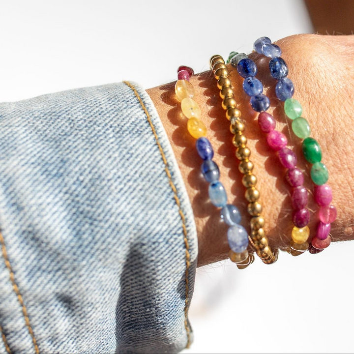 Close-up of a wrist wearing colorful beaded bracelets with a denim jacket sleeve.