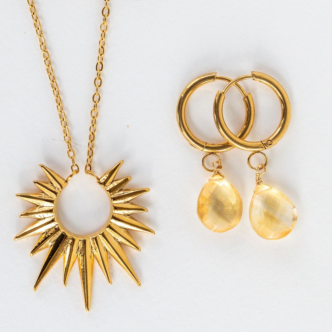 Gold Sun necklace and citrine earrings on a white background