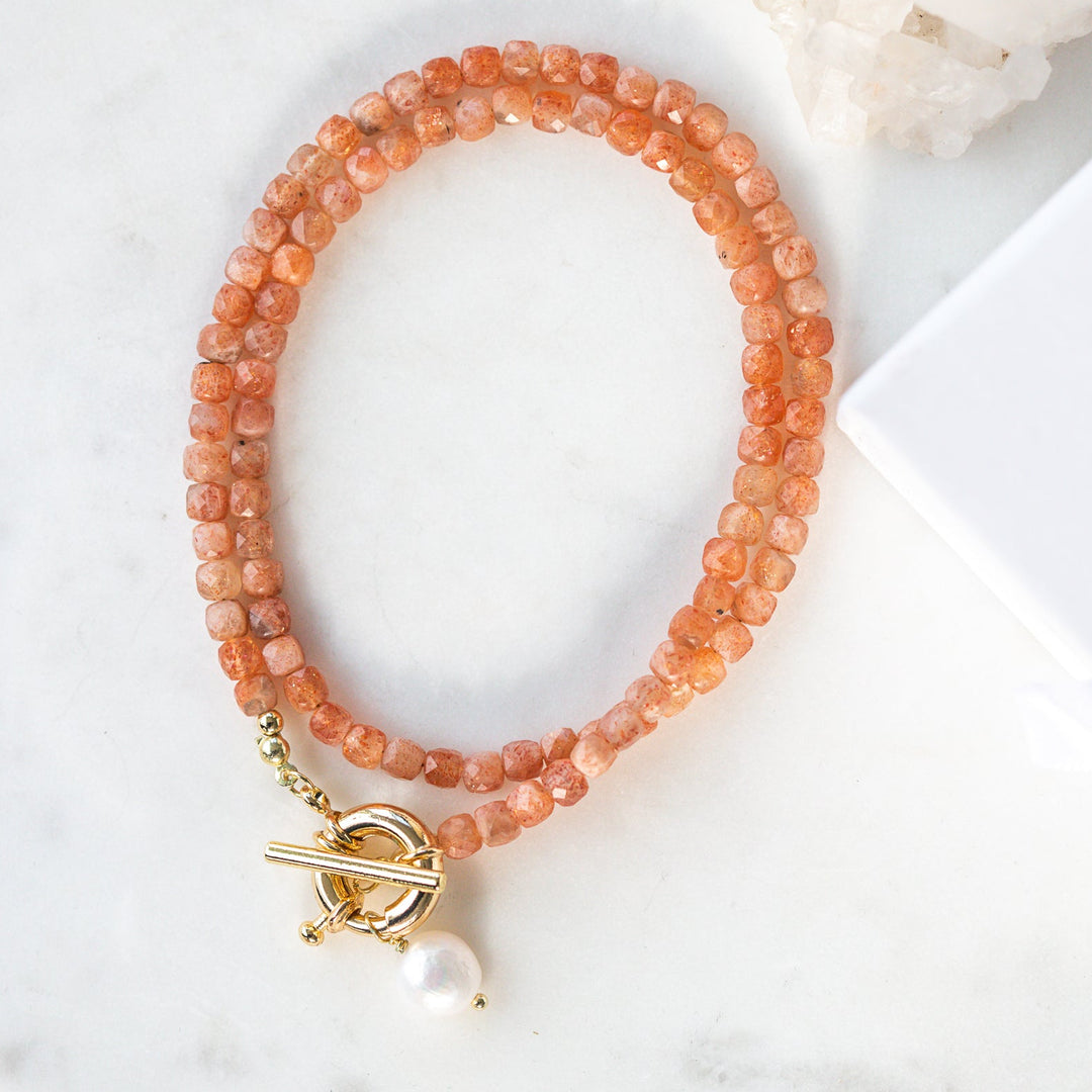 Peach-colored beaded necklace with a gold clasp and pearl charm on a white surface with 'Luna & Salt' packaging.