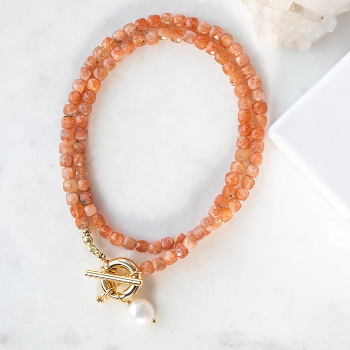 Peach-colored beaded necklace with a gold clasp and pearl charm on a white surface with 'Luna & Salt' packaging.